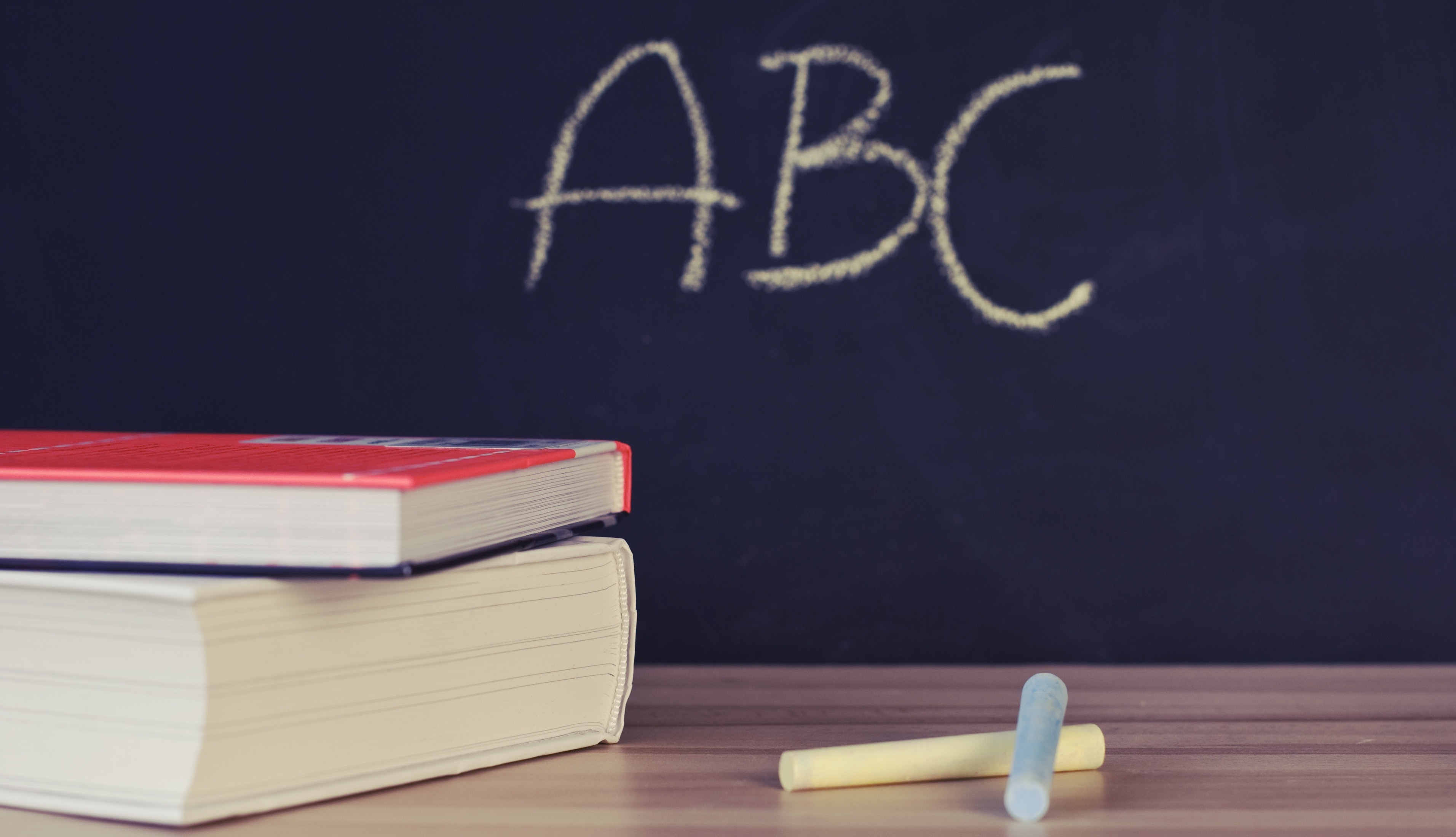 abc written on blackboard, two books on desk next two pieces of chalk